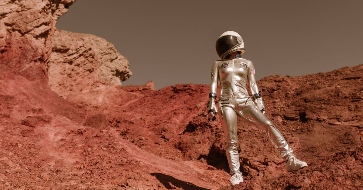 Astronaut in space suit standing on red rocky terrain resembling Mars' surface.